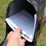 Hand placing mail in a black mailbox