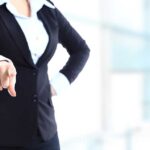 A professional woman in a suit pointing with her right hand