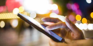 A persons hand using a smartphone in a city at night with blurred lights in the background