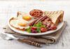A hearty breakfast plate featuring fried eggs, bacon, sausage, baked beans, toast, and salad