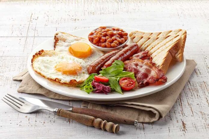 A hearty breakfast plate featuring fried eggs, bacon, sausage, baked beans, toast, and salad