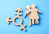 Women’s Privacy OBLITERATED – Court Rules Against Biology Wooden transgender symbol and couple figures on blue background.