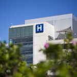 Modern hospital building with a prominent H sign against a clear blue sky