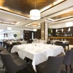 Interior of a modern restaurant with elegantly set tables and a bar area
