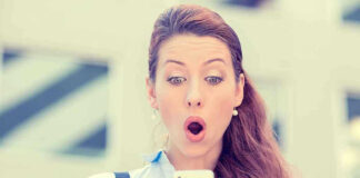 Surprised woman looking at her smartphone outdoors