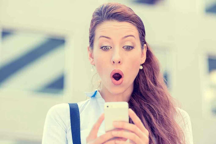 Surprised woman looking at her smartphone outdoors