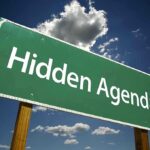 Road sign displaying the phrase Hidden Agenda against a blue sky