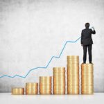 Businessman standing on stacks of coins, drawing a growth chart