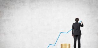 Businessman standing on stacks of coins, drawing a growth chart