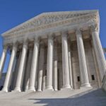 The Supreme Court building featuring grand columns and statues under a clear blue sky