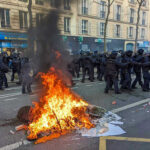 Protesters and police clash; fire in the street.