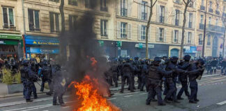 Protesters and police clash; fire in the street.