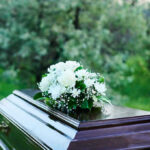 Coffin with white flowers outdoors in green surroundings.
