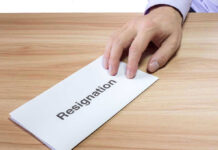 Hand holding a resignation letter on table.