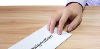 Hand holding a resignation letter on table.