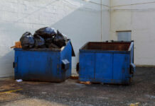 Dismembered Mom FOUND In Basement TRASH Two blue dumpsters, one overflowing with trash bags.