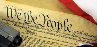 Close-up of the U.S. Constitution with a firearm and American flag