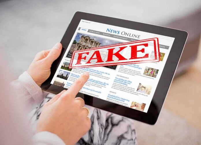 shutterstock_675861955 (1).jpg Person holding a tablet displaying a news website with a 'FAKE' stamp