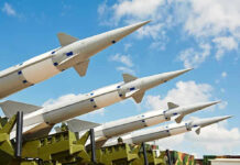 Multiple missiles pointed upward on launchers against blue sky.