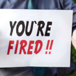 Person holding YOURE FIRED sign.