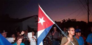 A group of people participating in a protest march holding a Cuban flag