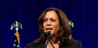 Woman speaking behind a podium with blue backdrop.