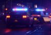 Police cars with flashing lights at a nighttime scene near a motel