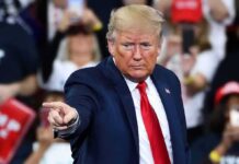 A man in a suit pointing during a speech at a rally